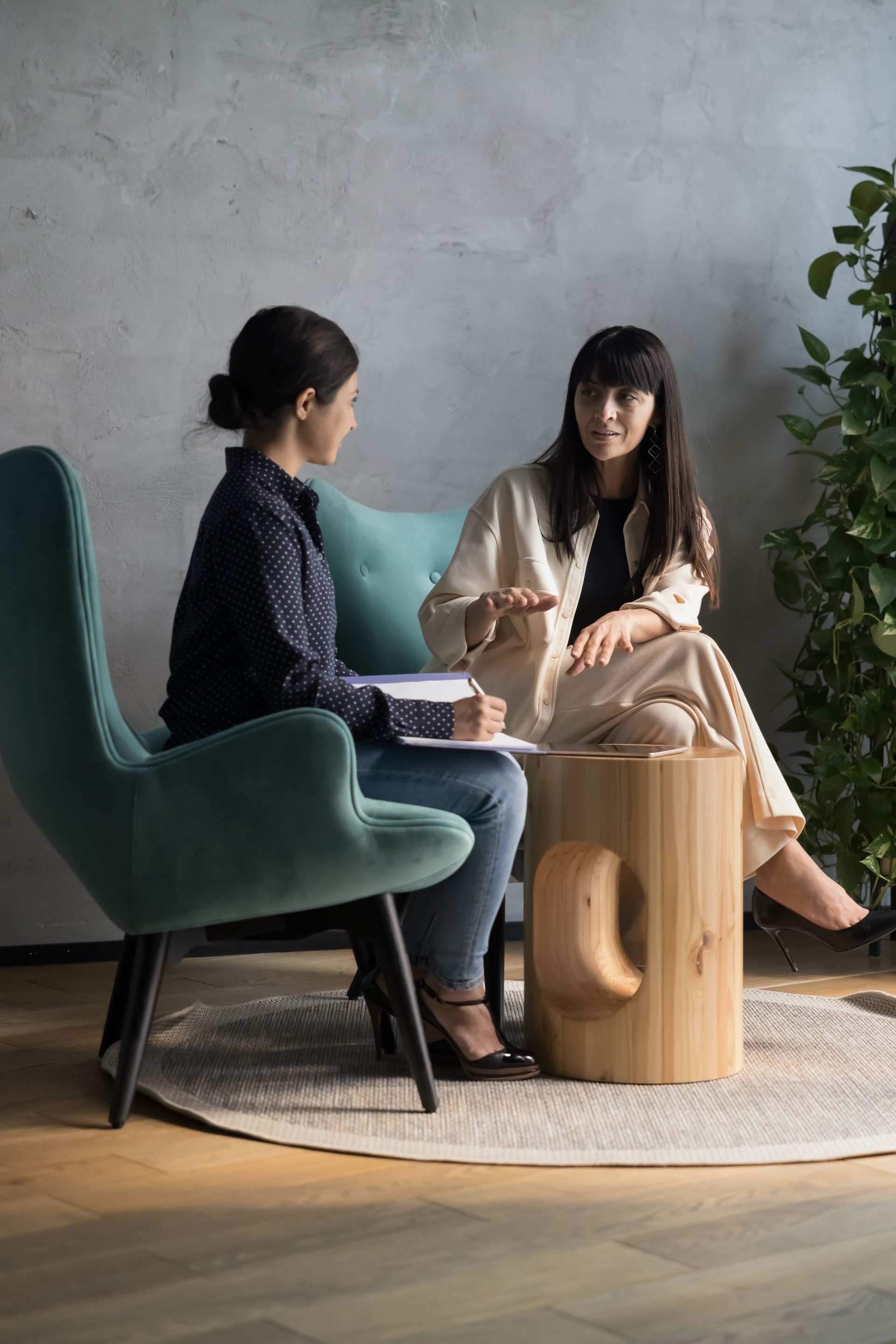 Two women talking seated on armchairs in office workspace